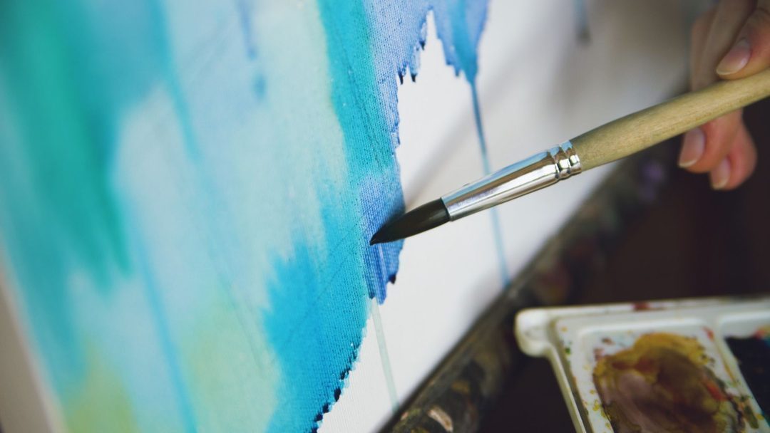 Main appliquant de la peinture bleue sur une toile